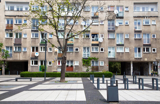 Weathered mid-century residential apartment block with balconies, satellite dishes and a tree in front of the building in Poland. Urban architecture reflecting post-war socialist housing devel