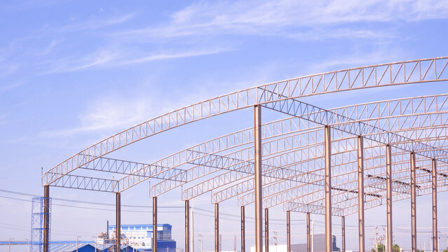 Steel roof truss structure under blue sky. Warehouse site construction. Industrial building in progress.