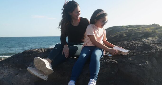 Happy latin mother having playful time with daughter using wood airplane on the beach - Holiday, summer and family lifestyle concept