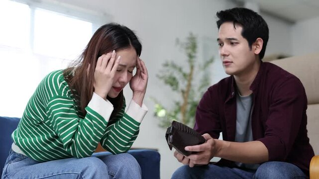 Young couple arguing about financial problems, showing empty wallet and unpaid bills on the table.