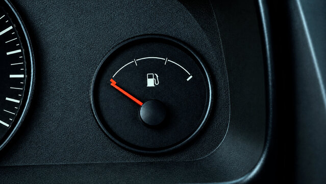 Close-up view of a vehicle's dashboard fuel gauge with a red indicator needle pointing near the empty mark on a dark textured console