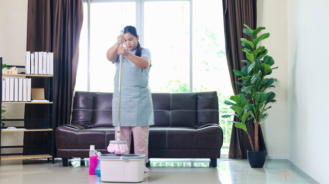 Professional female cleaner mopping a bright modern living room with a mop and bucket, representing house cleaning, housekeeping, home maintenance, hygiene, sanitation, domestic service, 