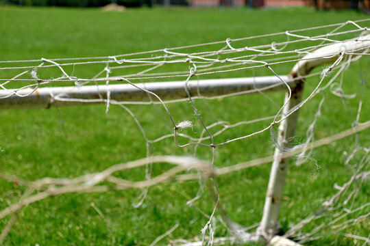 Selective focus close up of damaged torn threads of a soccer goal net with green grass blurred in background.