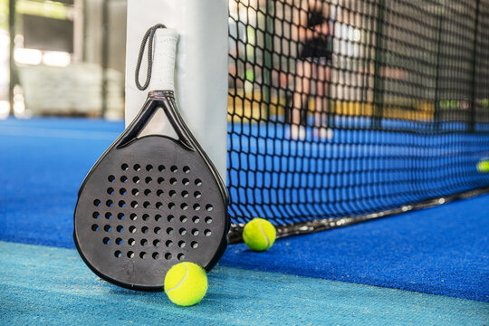 Padel racket leaning against a net on a professional court with yellow padel balls
