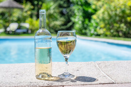 Glass and open bottle of white wine on concrete pool edge