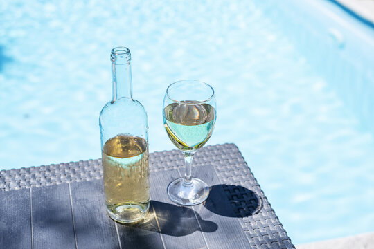 Glass and open bottle of white wine on concrete pool edge