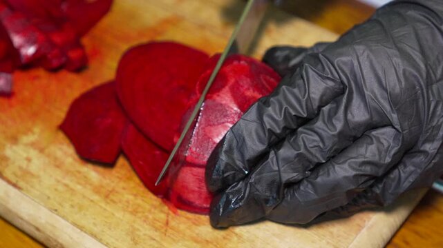 Beetroot slicing preparation. High-angle close-up shot of a chef using a sharp kitchen knife to cut fresh red vegetables on wood.