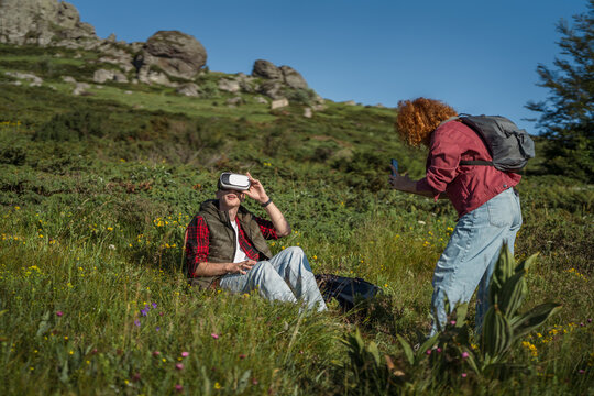 Man playing virtual reality game while woman films him outdoors