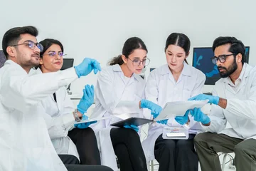 Five scientists in lab coats and gloves discussing documents and samples while seated in a circle, collaborative team meeting in bright research lab. © Jestercine