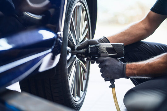 Mechanic using pneumatic wrench to change tyre in auto repair wo