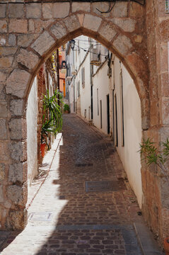 Portalet de la Juder&iacute;a, a medieval stone gateway leading into the historic Jewish Quarter of Sagunto, Valencia, Spain. A picturesque cobbled street preserves the charm and heritage.