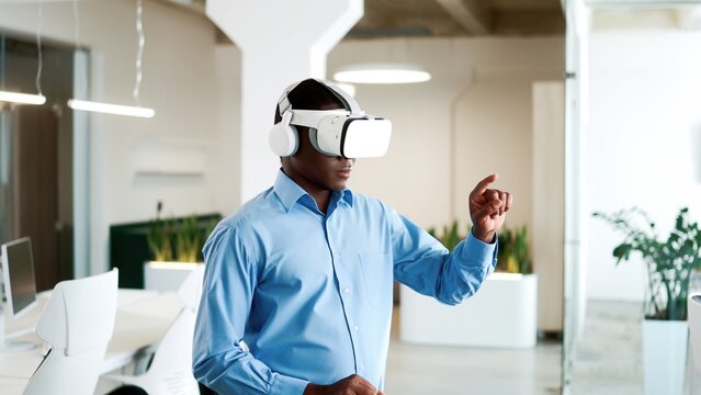 Close up portrait of young African American businessman working in modern big company office wearing VR glasses moving hands in air. Male boss works on a project using virtual reality headset
