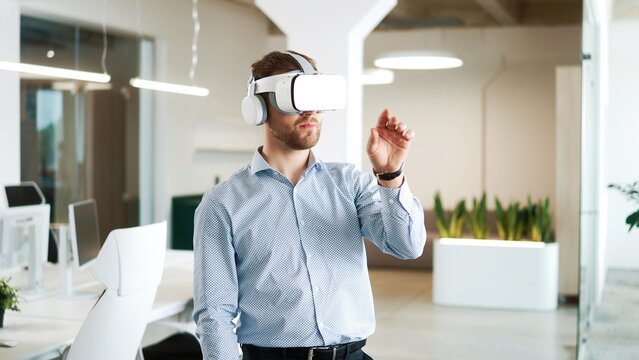 Close up portrait of Caucasian young man working in modern big company office wearing VR glasses moving hands in air. Businessman works on a project using virtual reality headset. Technology concept