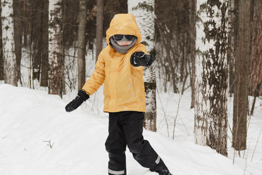 A child in a yellow jacket and gray hat plays in a winter park. A snowy winter forest, a fairy tale. An active, healthy lifestyle and fun games in the snow during the holidays