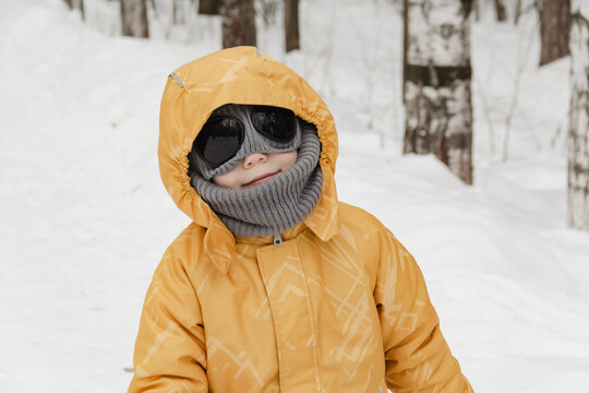 A child in a yellow jacket and gray hat plays in a winter park. A snowy winter forest, a fairy tale. An active, healthy lifestyle and fun games in the snow during the holidays