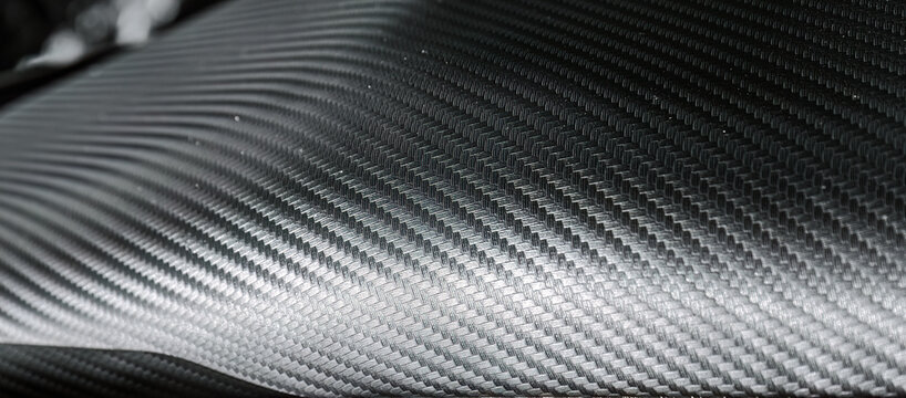 Close view of black carbon fiber style surface showing woven structure and reflective texture. Useful for automotive design, technology themes, engineering projects, and modern backgrounds.