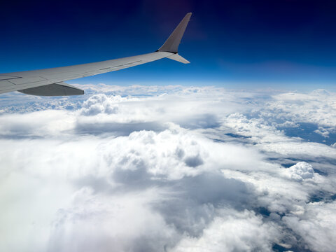 Plane wing soars above fluffy white clouds