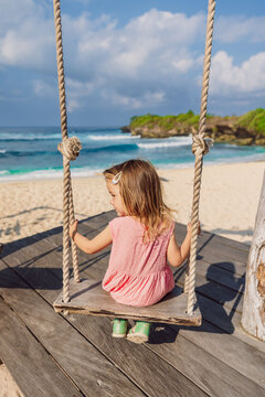 Little girl plays and swinging on swings on beach with ocean, enjoy childhood