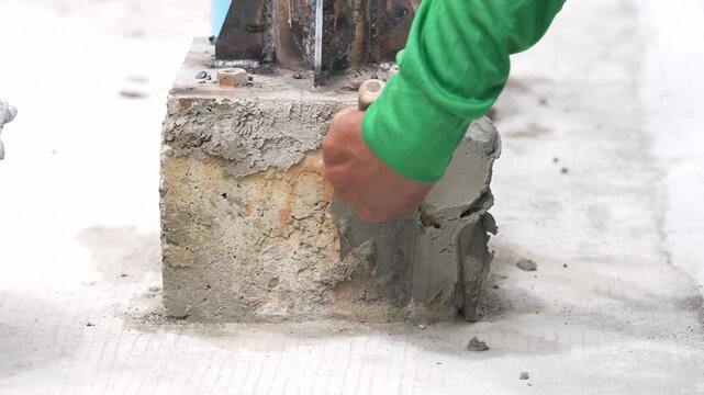 Concrete repair mason trowel cement construction foundation steel column hand applying fresh mortar plaster on damaged concrete pedestal base during building renovation maintenance closeup
