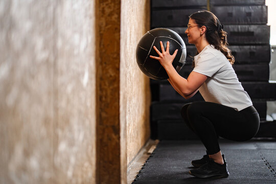Woman performing a wall squat with a medicine ball in a gym