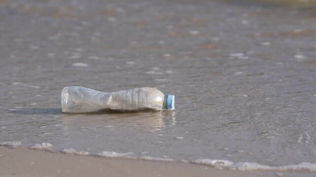 Plastic bottle on beach sand and shoreline, ocean pollution, litter and waste near foam waves marine debris and trash from discarded container highlight harm, human impact, urgent coastal cleanup