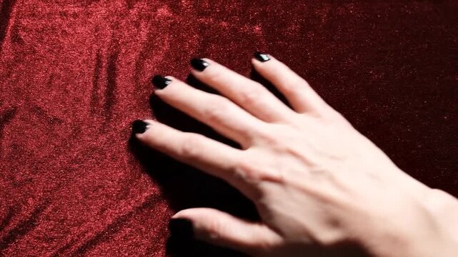Overhead shot of a hand with black nail polish stroking rich red velvet fabric in two directions showcasing luxurious texture