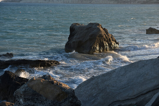 Sea rock surrounded by crashing sea foam on a sandy beach at golden hour, Cyprus