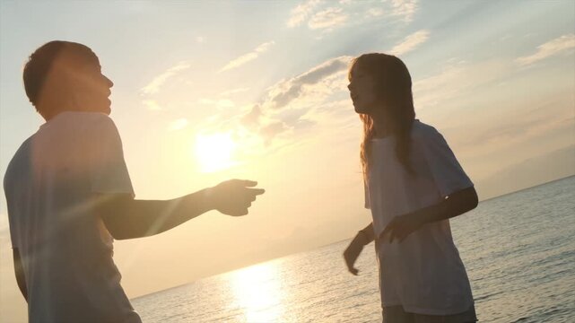 Caucasian teenage boy and girl argue on the seashore at sunset, using expressive hand gestures like rap battle and freestyle rap. Youth trends, street culture, emotional communication.