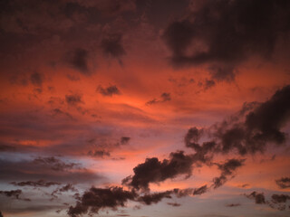 Fototapeta premium Sunset featuring deep red and orange hues contrasting with dark-textured clouds suitable for a wallpaper or background.