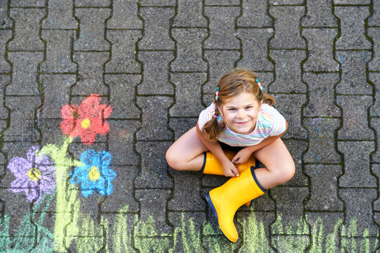 Cute little girl and flowers painted with colorful chalks on asphalt. Happy preschool child having fun with painting chalk picture. Creative leisure for children, drawing and painting.