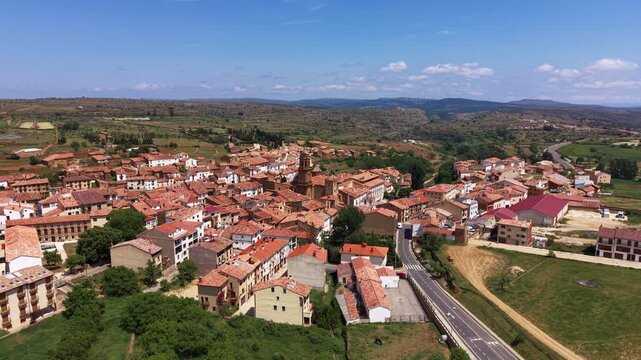 La Iglesuela del Cid in Maestrazgo, Teruel, Spain, with a baroque clock tower rising above terracotta-roofed stone buildings on an arid plateau under blue sky