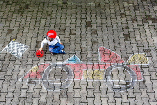 Happy healthy little boy having fun with racing car picture drawing with chalk. Creative leisure for children. Adorable kid child sitting on asphalt creating and playing with colorful chalks.