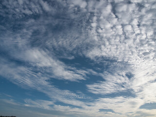 Clear blue sky with thin white clouds forming patterns resembling fish scales or ripples—specifically cirrocumulus clouds often referred to as a buttermilk sky. © saksuvan