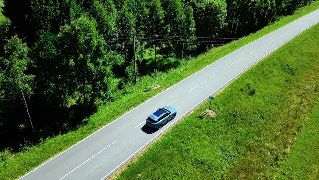 Car traveling along a scenic road bordered by vibrant greenery under bright sunlight