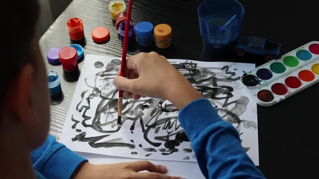child painting with black watercolor on white paper. Concept of children's emotional expression, anxiety, fears, emotional wellbeing, art therapy, psychological assessment, creativity, stress, mental 