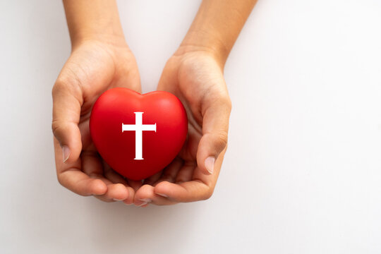 Childhood and religion. Christianity, faith. A child's hands holding a heart with a cross