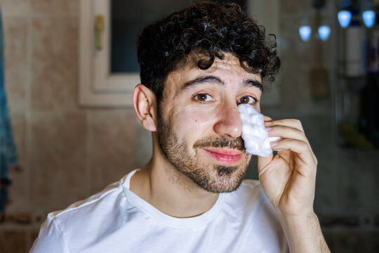 Young man performing self-care skincare routine with cotton pad in bathroom