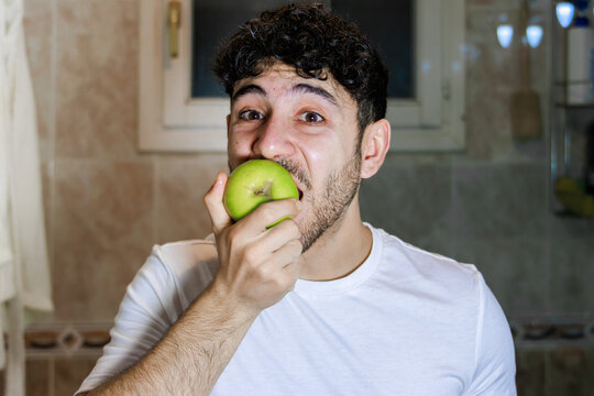 Young man enjoying a fresh green apple, practicing selfcare and healthy eating