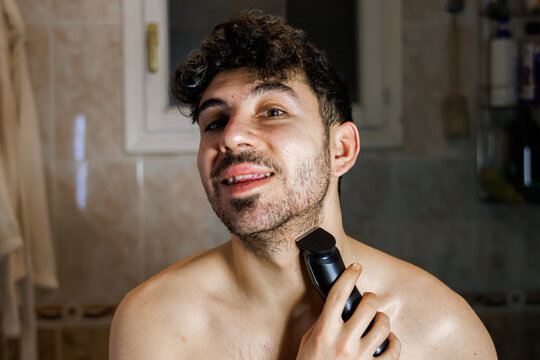 Man using an electric trimmer on his beard, maintaining personal grooming and selfcare
