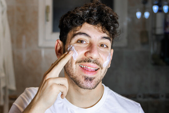 Man applying skincare cream to his face, performing a daily grooming routine