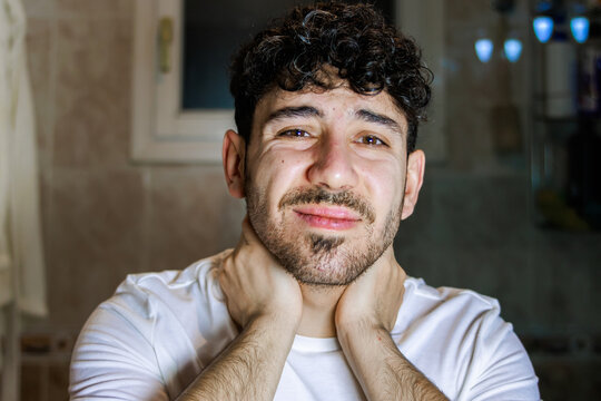 Young man smiling and touching his neck, enjoying self-care and morning routine