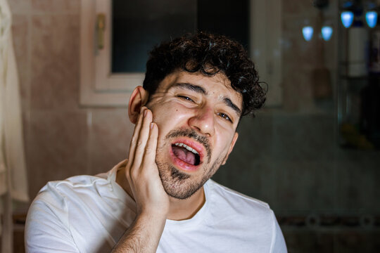 Young man suffering from toothache, holding cheek in pain, dental problem