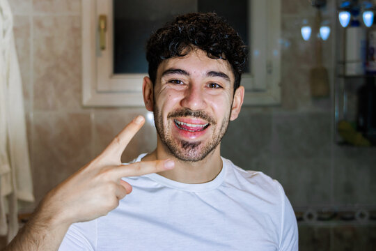 Young man smiling in bathroom showing peace gesture at morning selfcare routine
