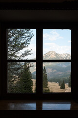 Obraz premium Scenic Mountain View Framed Through a Dark Wooden Cabin Window. A cozy view looking out through a dark wooden window frame towards a beautiful mountain landscape