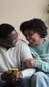 Joyful black couple watching smartphone and laughing
