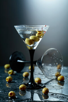 Green olives and glass of martini on a black stone table.