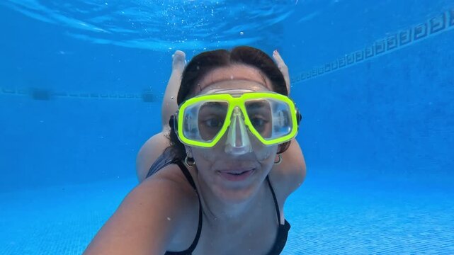 Happy teenage girl wearing a snorkel mask taking a selfie video while swimming underwater in a blue pool on vacation