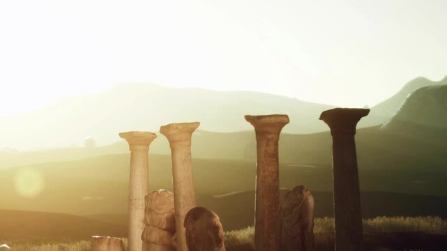 Stone columns are visible in a grassy field at sunset. Mountains loom in the background. The sun casts a warm glow on the scene. Nature surrounds the ancient ruins.