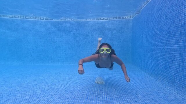 Teenage girl swims, smiling underwater in the pool