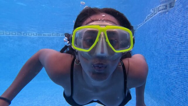 Young woman moves gracefully through pool water while wearing bright goggles